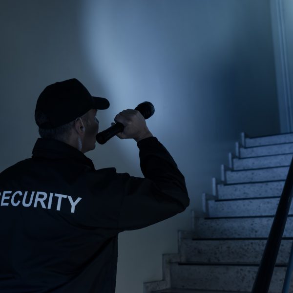 Rear view of security guard searching on stairway with flashlight in office building